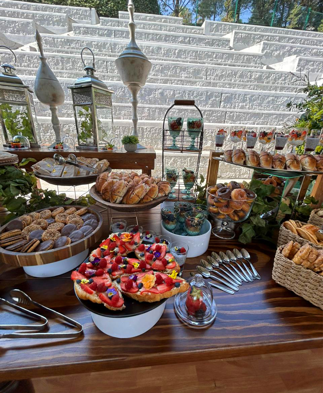 Servicio de banquetes y coffee break con una variedad de alimentos, incluyendo pasteles de frutas, galletas, sándwiches y postres. Decoración con linternas y elementos naturales, ideal para eventos.